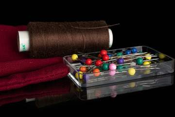 One whole haberdashery item spool on cloth with needles isolated on black glass
