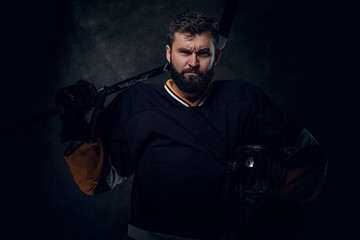 Portrait of brutal bearded man in hockey player uniform at dark photo studio.