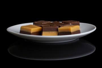 Group of six whole sweet brown caramel chocolate candy on white ceramic plate isolated on black glass