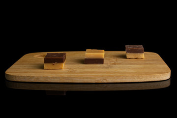 Group of three whole sweet brown caramel chocolate candy on bamboo cutting board isolated on black glass