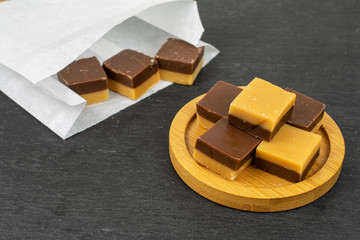 Group of eight whole sweet brown caramel chocolate candy on bamboo coaster in paper bag on grey stone