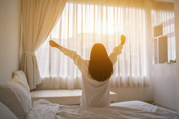Beautiful Asian woman waking up on her bed in the bedroom, she is stretching and smiling after wake...