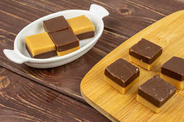 Group of eight whole sweet brown caramel chocolate candy in white oval ceramic bowl on bamboo cutting board on brown wood