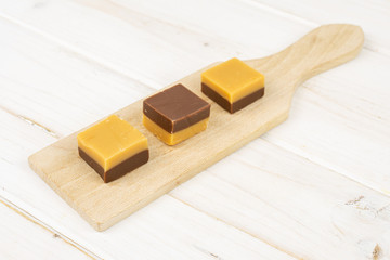 Group of three whole sweet brown caramel chocolate candy on small wooden cutting board on white wood