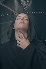 young very angry man with a caucasian face is dressed in a black robe and leather big boots and...