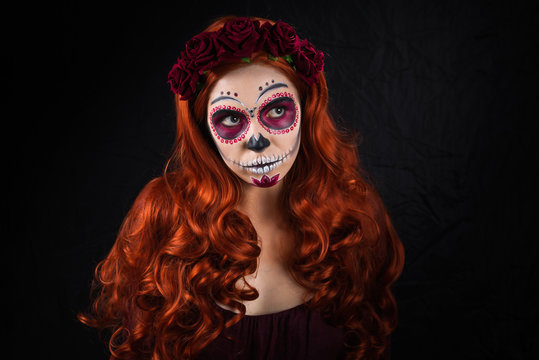 Woman with sugar skull makeup and red hair isolated on black background. Day of the dead. Halloween.