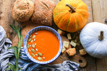 Vegetarian autumn pumpkin cream soup with seeds. Seasonal autumn food - pumpkin soup with thyme. Pumpkin soup with herbs, cream, breadcrumbs and parmesan, served in a bowl, top view. Place for text