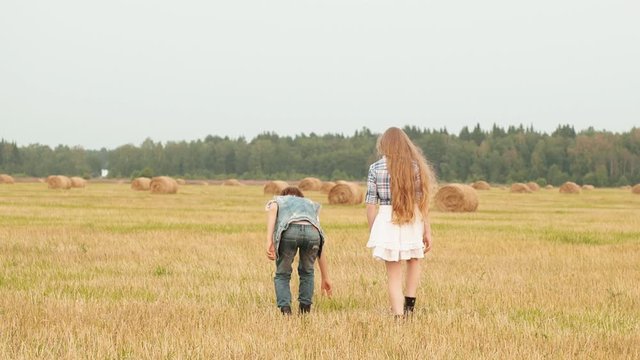 Teenager girl and boy walking on harvesting field on haystack background. Happy girl and boy having fun on countryside field in village. Funny teen couple walking on autumn meadow