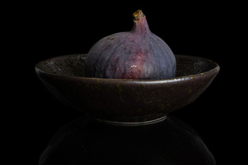 One whole fresh purple fig in dark ceramic bowl isolated on black glass