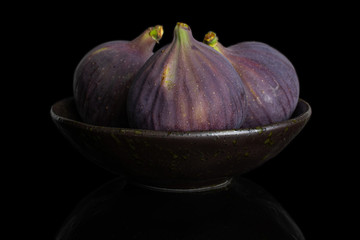 Group of three whole fresh purple fig in dark ceramic bowl isolated on black glass