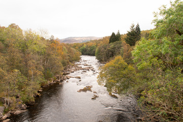 Scenic autumnal view in Scotland. View of colorful forest and River Tummel seen from old brick stone bridge in Pitlochry in the area of Perth and Kinross in Scotland. Overcast day.