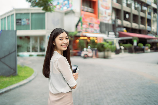 Young Asian Chinese business woman smiling and use digital tablet computer outdoor near office building,She has long black hair ,happiness girl with Summer sunny lifestyle fashion portrait on street