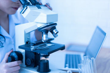 Asian female doctor working on laptop with a microscope for an exam at hospital giving patient convenience online service advice, smiling write a prescription , healthcare, preventing disease concept