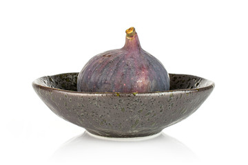 One whole fresh purple fig in dark ceramic bowl isolated on white background