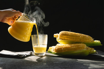 The steam from a jug and a glass of corn milk on black background, Warm drinks make good...