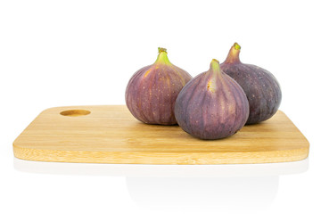 Group of three whole fresh purple fig on bamboo cutting board isolated on white background