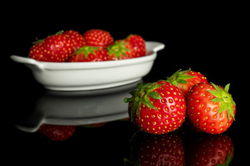 Group of nine whole fresh red strawberry in white oval ceramic bowl isolated on black glass