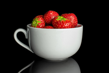 Lot of whole fresh red strawberry in white ceramic cup isolated on black glass