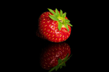 One whole fresh red strawberry isolated on black glass