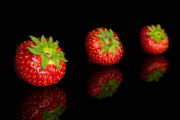 Group of three whole fresh red strawberry isolated on black glass