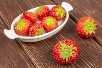 Group of eight whole fresh red strawberry in white oval ceramic bowl on brown wood