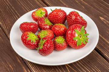 Lot of whole fresh red strawberry on white ceramic plate on brown wood