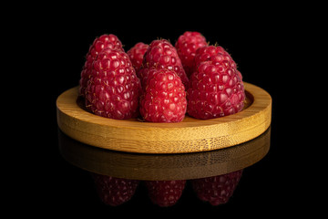 Lot of whole fresh red raspberry on bamboo coaster isolated on black glass