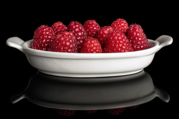 Lot of whole fresh red raspberry in white oval ceramic bowl isolated on black glass