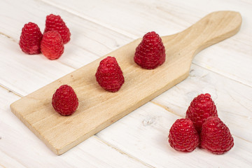 Group of nine whole fresh red raspberry on small wooden cutting board on white wood