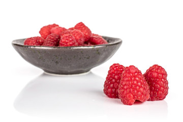 Lot of whole fresh red raspberry in dark ceramic bowl isolated on white background