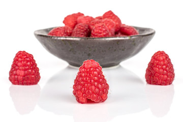 Lot of whole fresh red raspberry in dark ceramic bowl isolated on white background