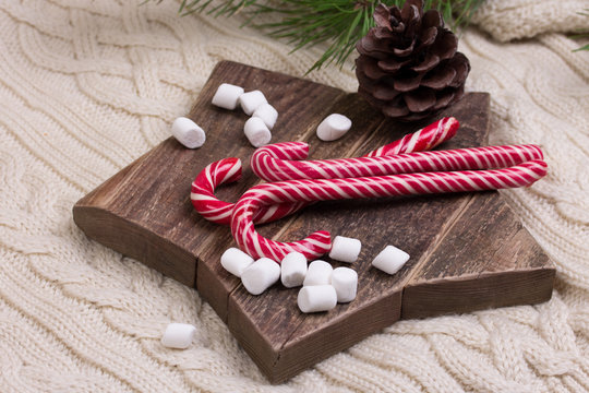 Christmas composition. Spruce branches, candy cane and Marshmallow on a star-shape wooden cutting board.