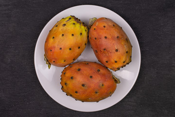 Group of three whole fresh orange opuntia on white ceramic plate flatlay on grey stone