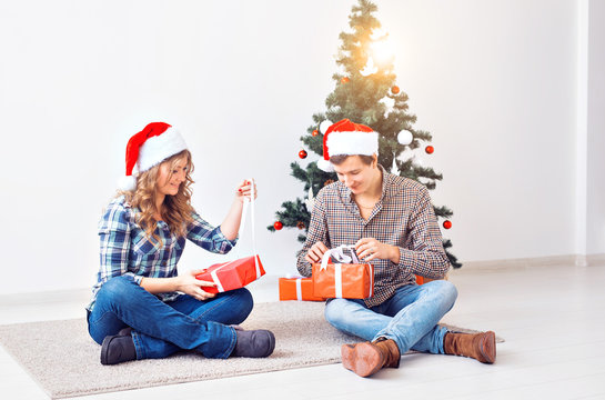 Holidays, christmas and family concept - Young happy couple opening gifts at home.