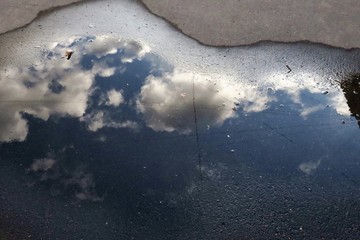 reflection of the sky with clouds in a puddle on the pavement