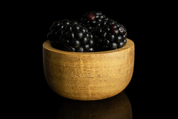 Group of four whole fresh black blackberry in tiny wooden bowl isolated on black glass