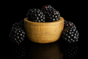 Group of six whole fresh black blackberry in tiny wooden bowl isolated on black glass