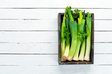 Fresh leeks in a wooden box on a white wooden background. Top view. Free copy space.