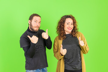 Beautiful young couple over green isolated background doing ok sign, thumb up with fingers, excellent sign