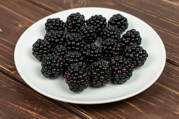 Lot of whole fresh black blackberry on white ceramic plate on brown wood