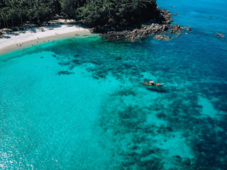 Fototapeta na wymiar Drone view of the lagoon: narrow strip of the white sand, clear blue water and a small boat, green hills covered with tropical forest; paradise concept.
