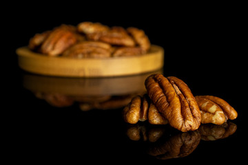 Lot of whole dry brown pecan nut on bamboo coaster isolated on black glass