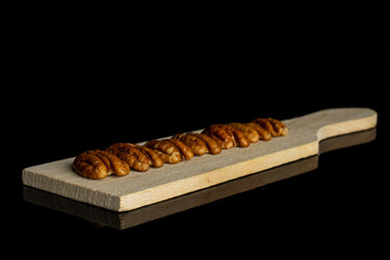 Group of seven whole dry brown pecan nut on small wooden cutting board isolated on black glass