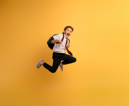 Young boy student runs fast to escape from school. Yellow background