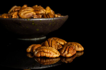 Lot of whole dry brown pecan nut in dark ceramic bowl isolated on black glass