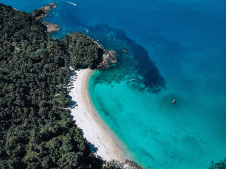 Top view of the exotic lagoon: narrow strip of the white sand framed with turquoise clear sea from one side and green tropical forest from another; paradise concept.