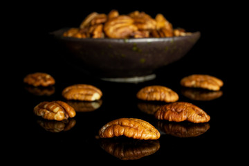 Lot of whole dry brown pecan nut in dark ceramic bowl isolated on black glass
