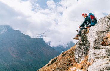 Young hiker backpacker female sitting on cliff edge and enjoying the Imja Khola valley during high altitude Everest Base Camp (EBC) trekking route near Phortse, Nepal. Active vacations concept image.