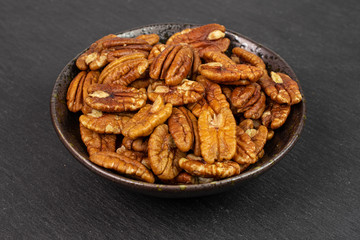 Lot of whole dry brown pecan nut in dark ceramic bowl on grey stone