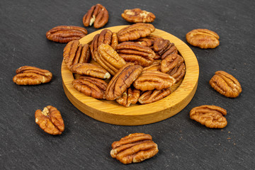 Lot of whole dry brown pecan nut on bamboo coaster on grey stone